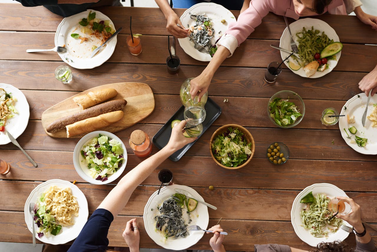 about-us-01 An overhead shot of a dining table featuring various pasta dishes and salads shared by a group.